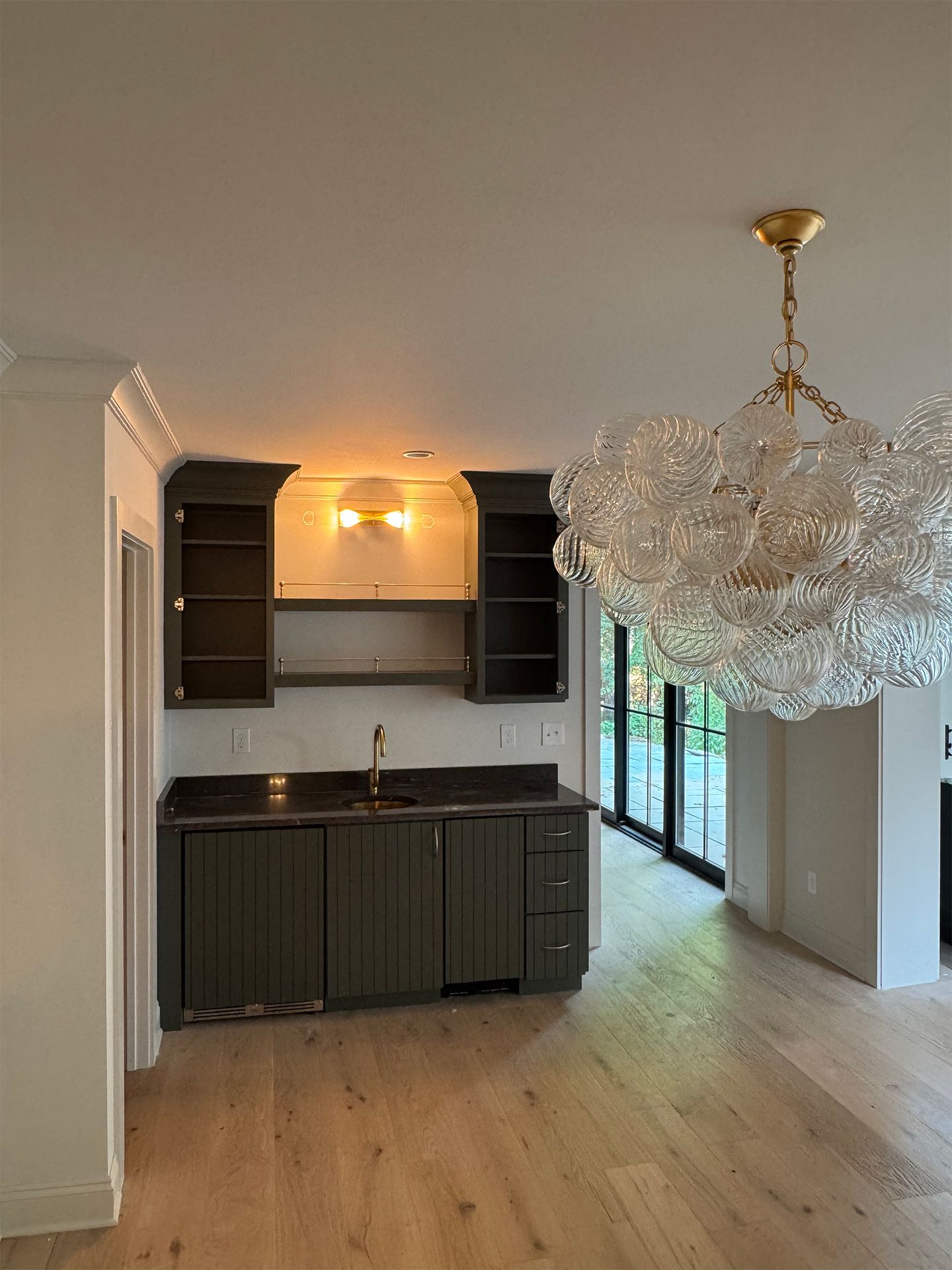 Small kitchen with dark cabinets, light wood floors, and a large crystal chandelier in a bright room.