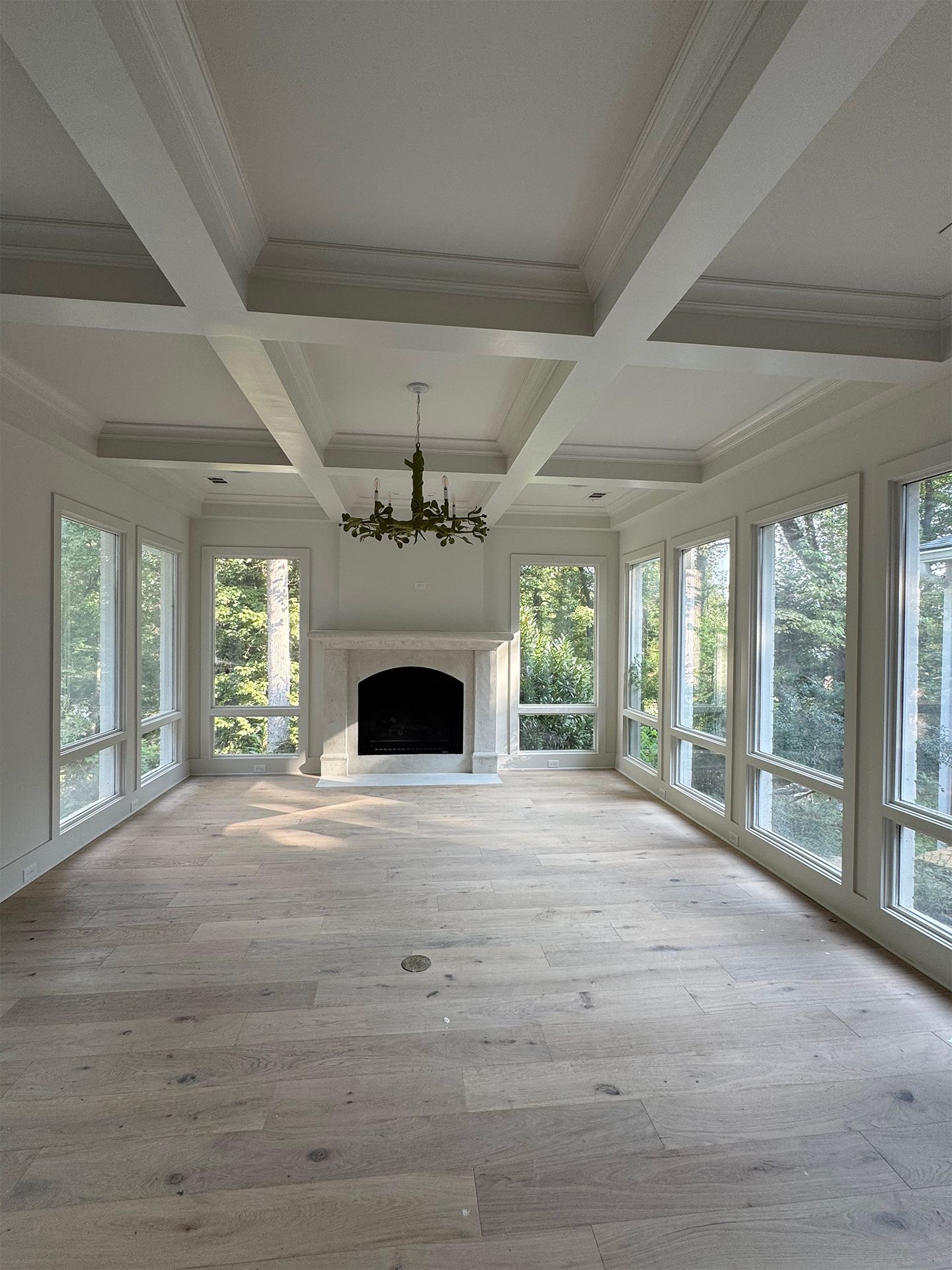 Empty sunroom with large windows, white coffered ceiling, and a fireplace at the far end.