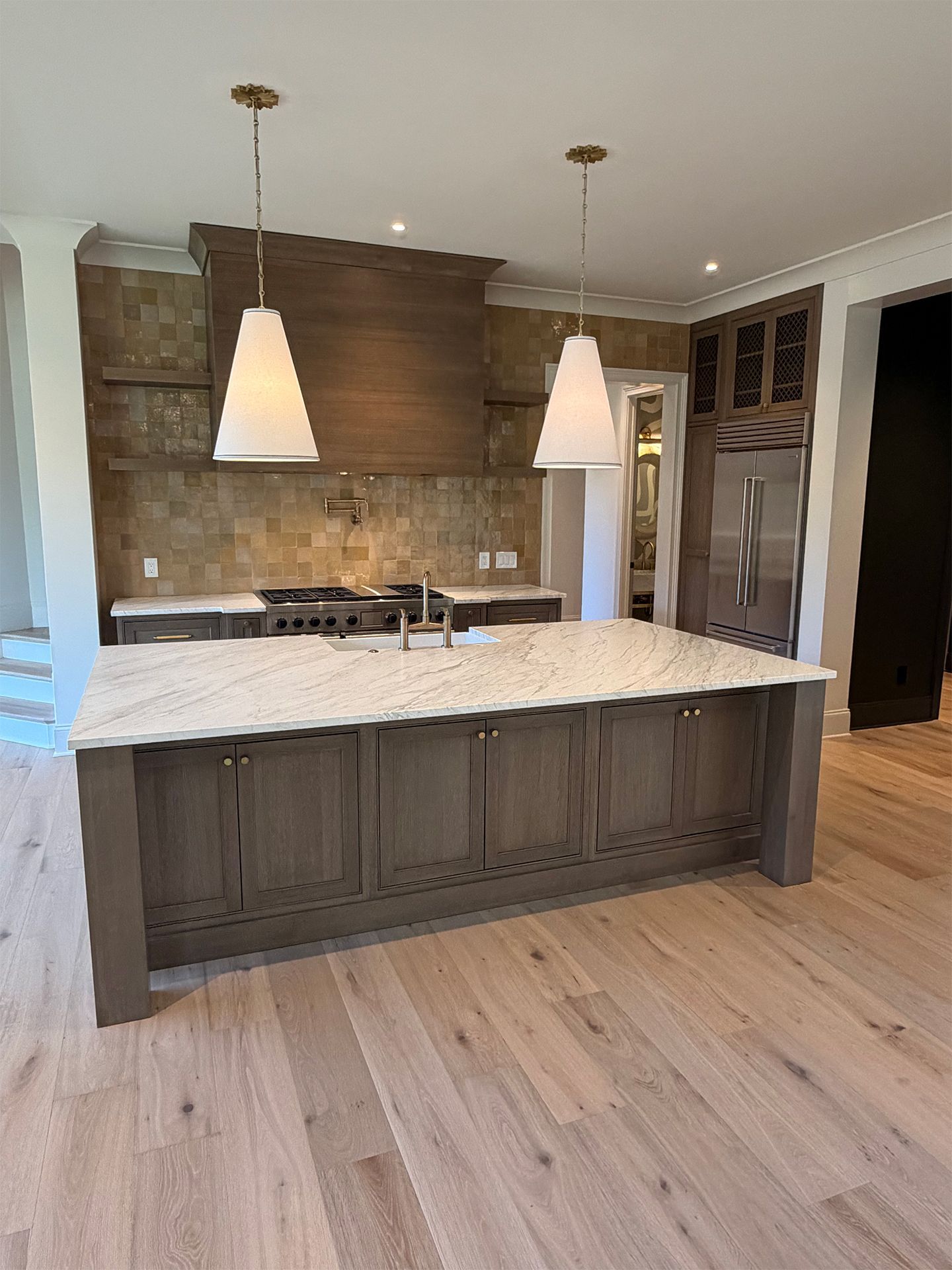 Modern kitchen with large island, pendant lights, stone backsplash, and light wood flooring