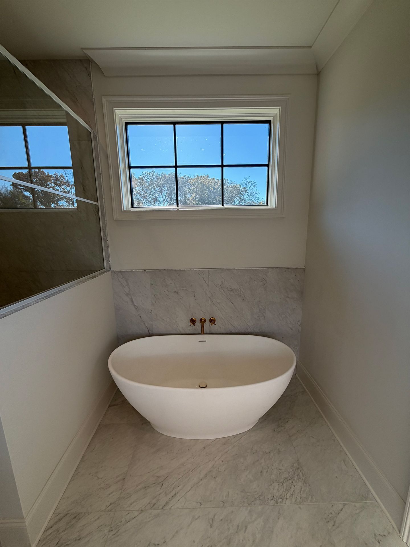 Modern bathroom with freestanding white tub beneath a window and marble tile walls