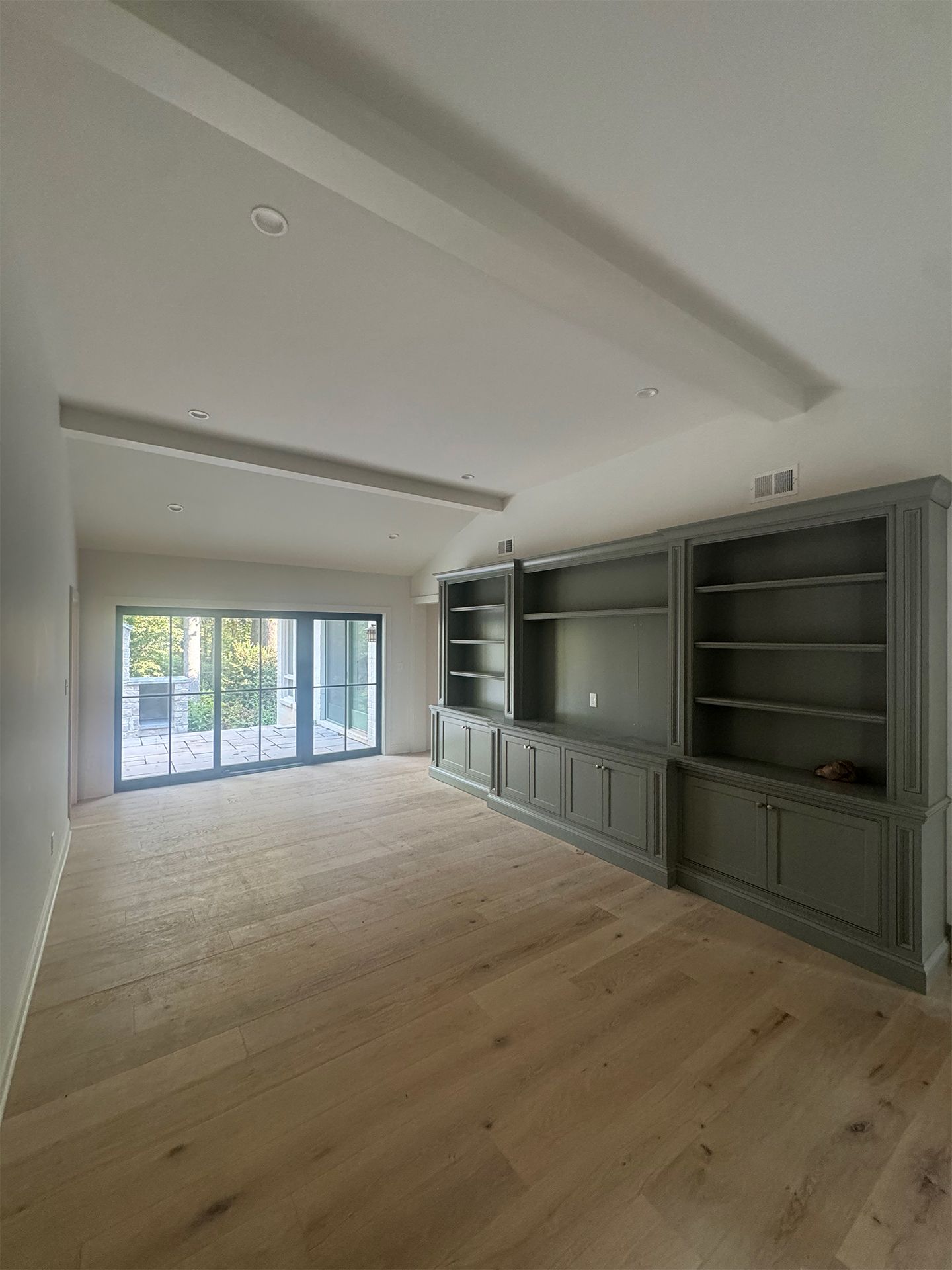Empty modern living room with wood floors, built-in gray cabinets, and large sliding glass doors opening to a balcony.