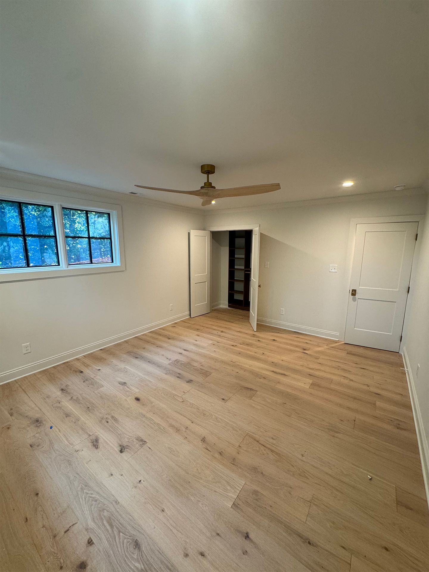Empty room with light wood floors, white walls, a window, ceiling fan, and closet doorway.