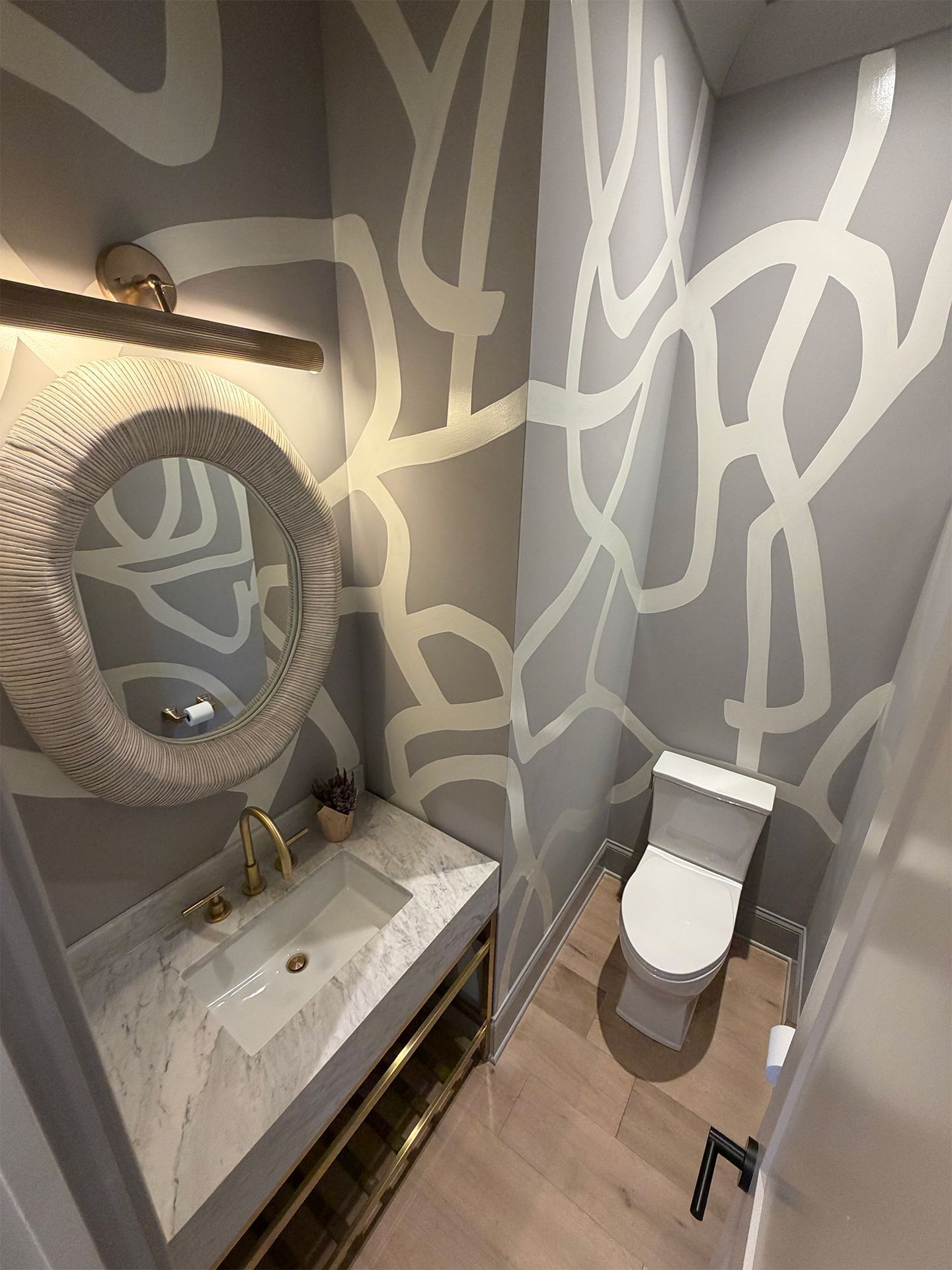 Modern bathroom with patterned walls, round mirror, floating sink, and toilet.