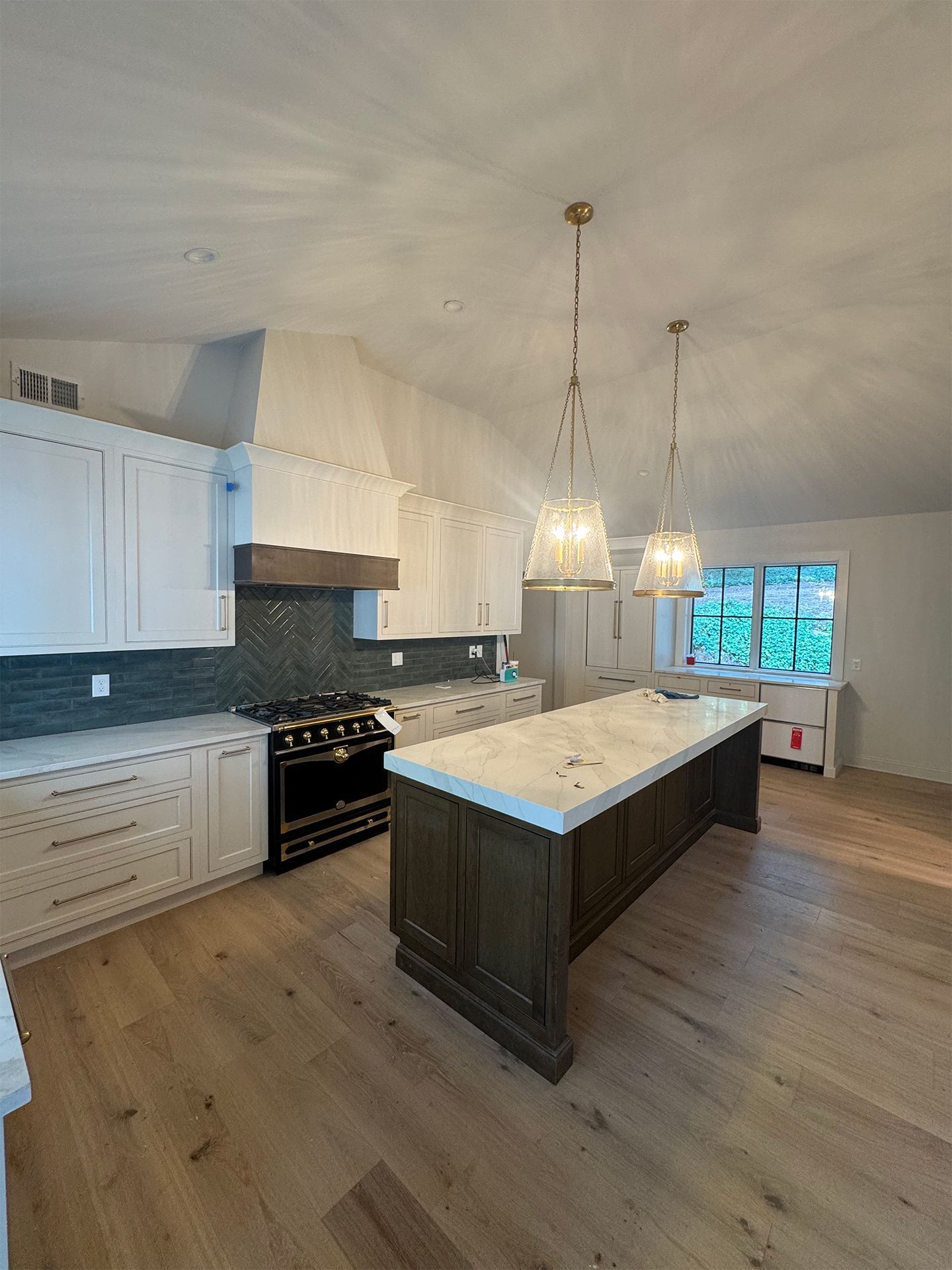 Modern kitchen with white cabinets, dark island, pendant lights, and large window.