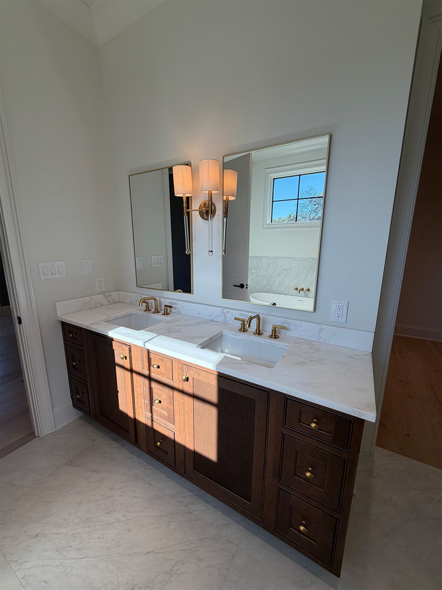 Modern double vanity bathroom with white counters, dark cabinets, mirrors, and wall sconces