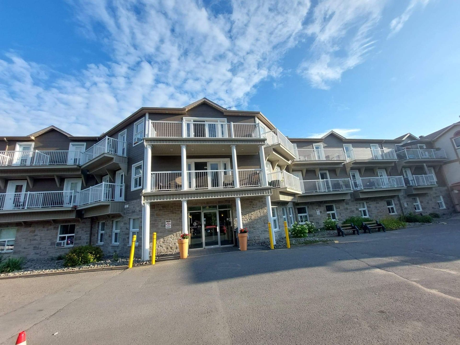 A three-story hotel building with stone lower walls, gray siding, and tiered balconies under a blue, cloudy sky.