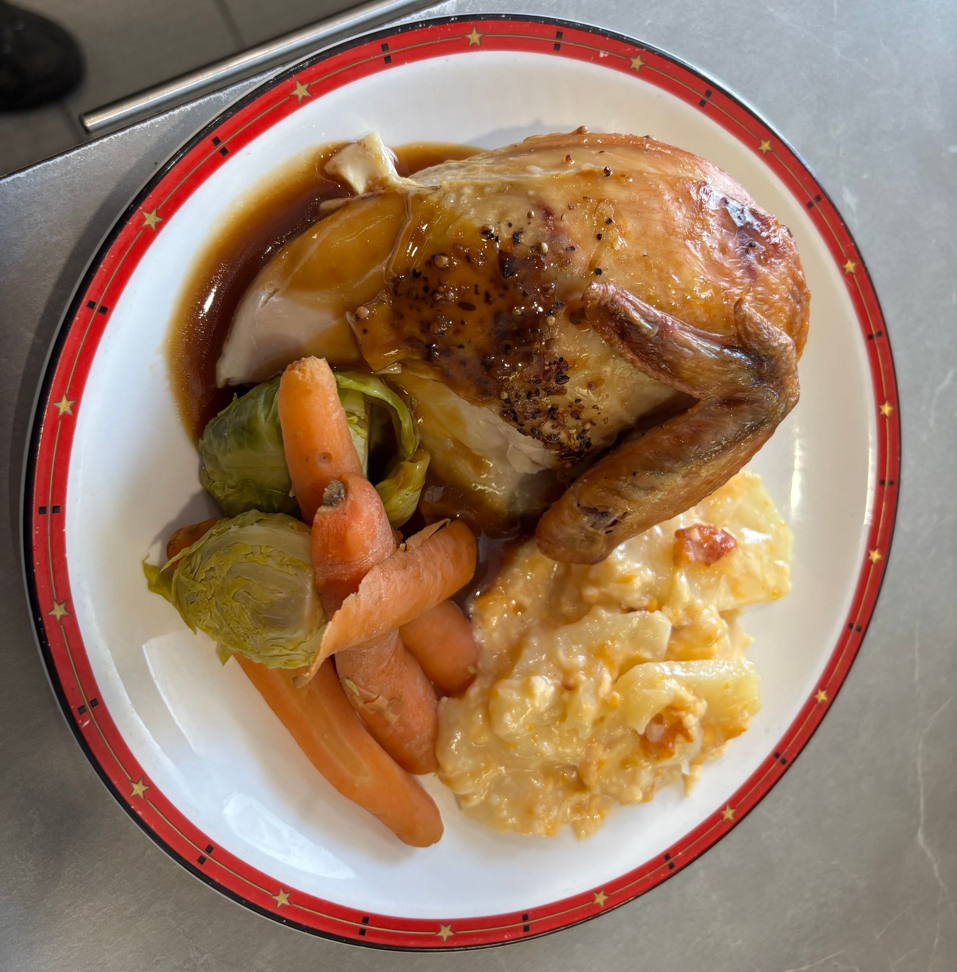 A roasted chicken dinner served on a plate with Brussels sprouts, carrots, and creamy potatoes with gravy.