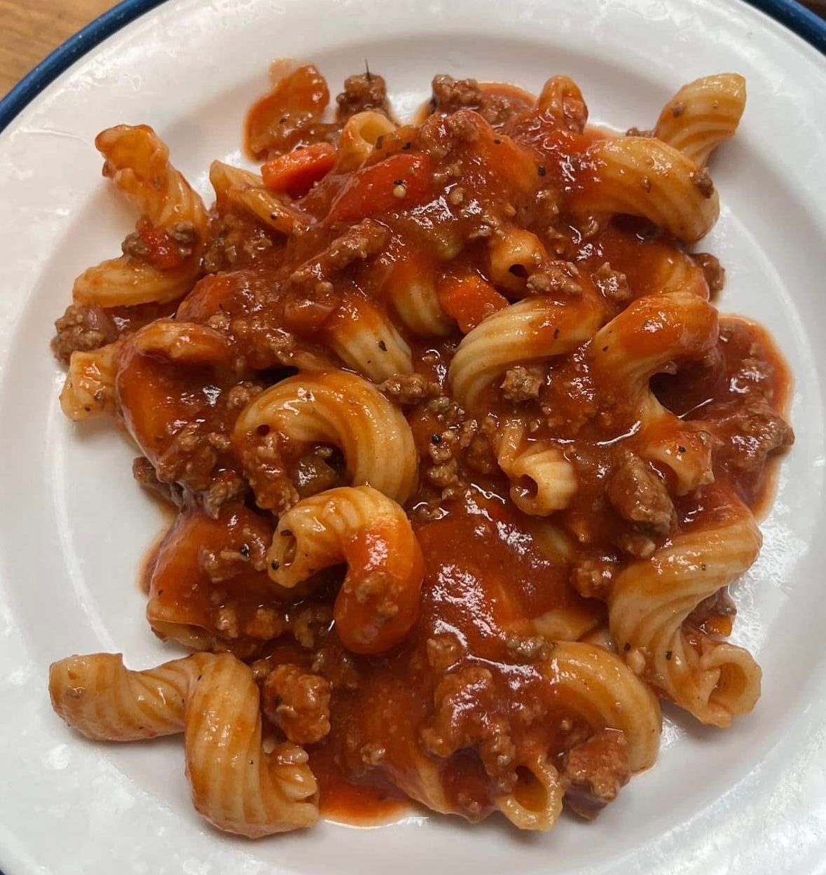 A serving of spiral-shaped pasta tossed in a thick, meat-based red tomato sauce on a white plate.