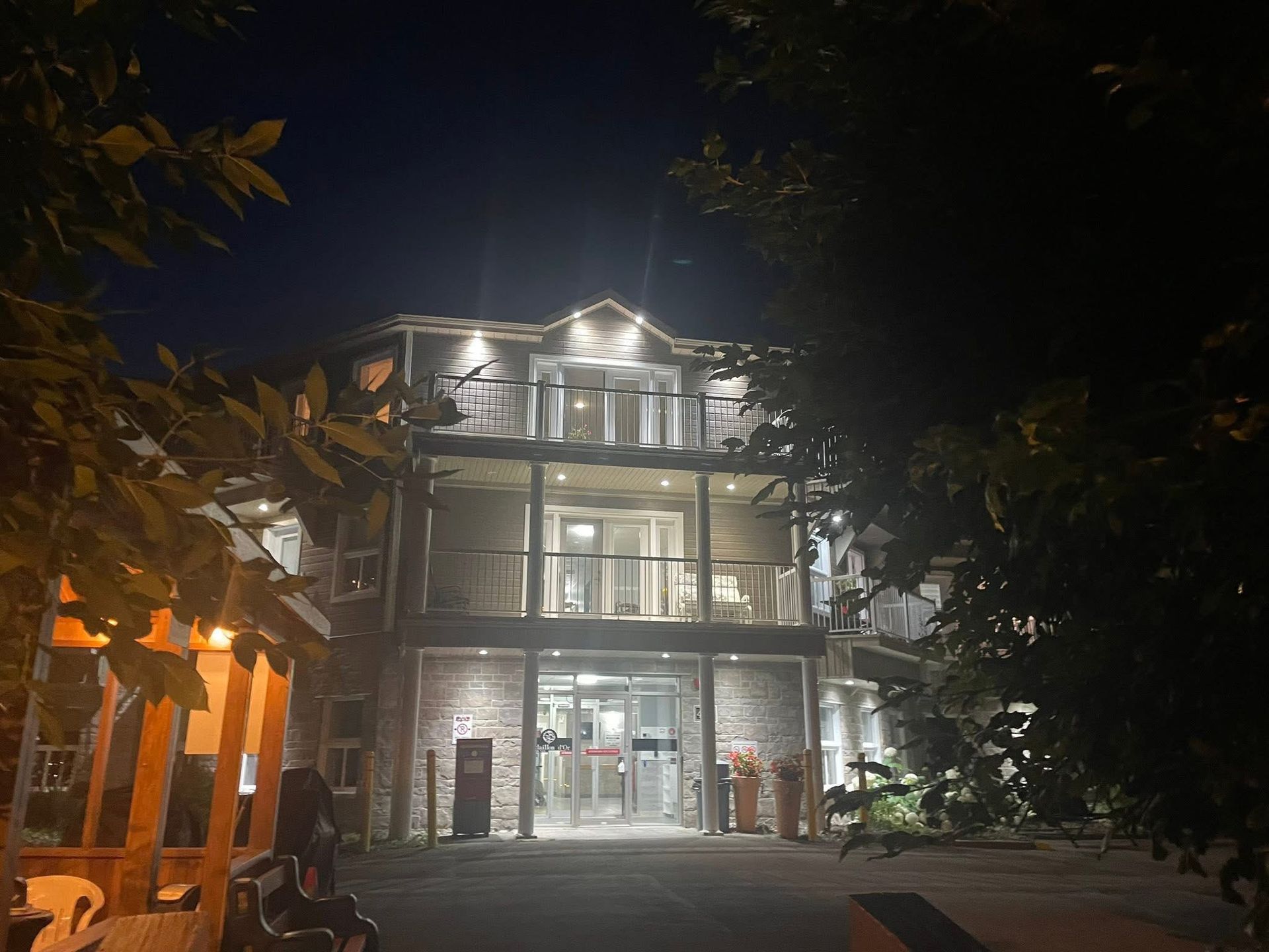 A multi-story hotel with lit balconies at night, viewed from a tree-lined driveway.