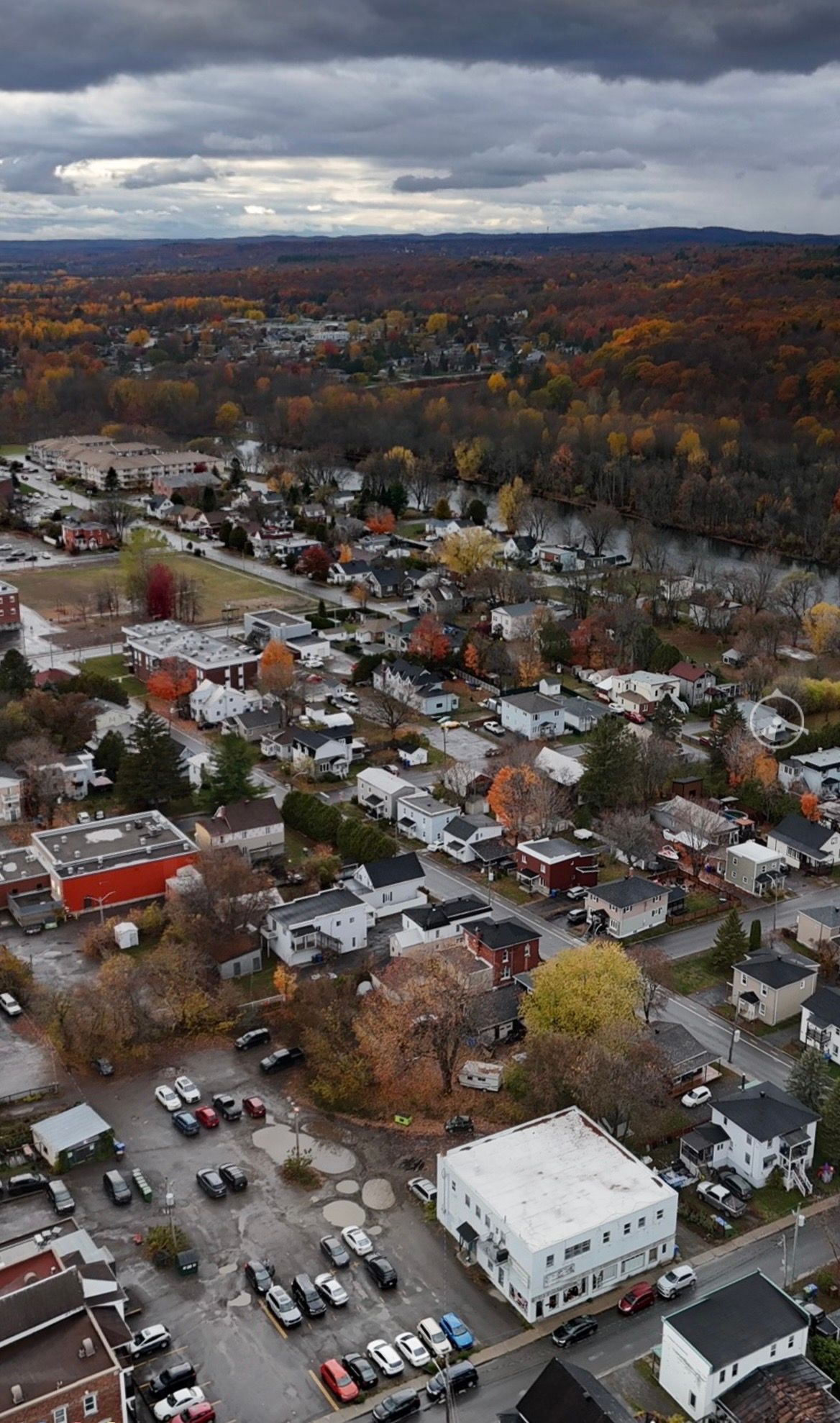Aerial view of a residential neighborhood during autumn, featuring colorful trees, houses, and a parking lot.