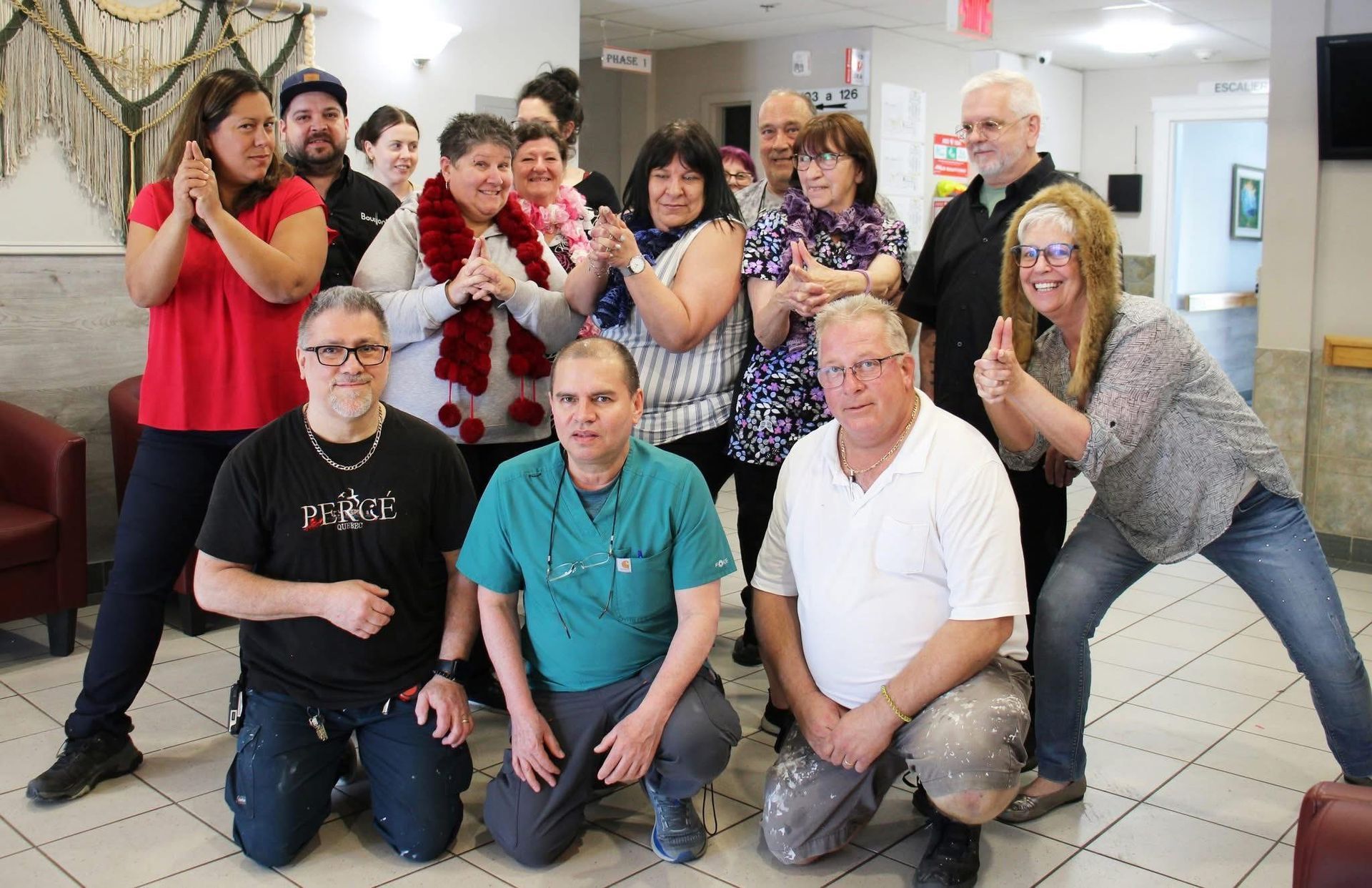 A diverse group of people posing playfully in a lobby, with some forming hand gestures and smiling at the camera.