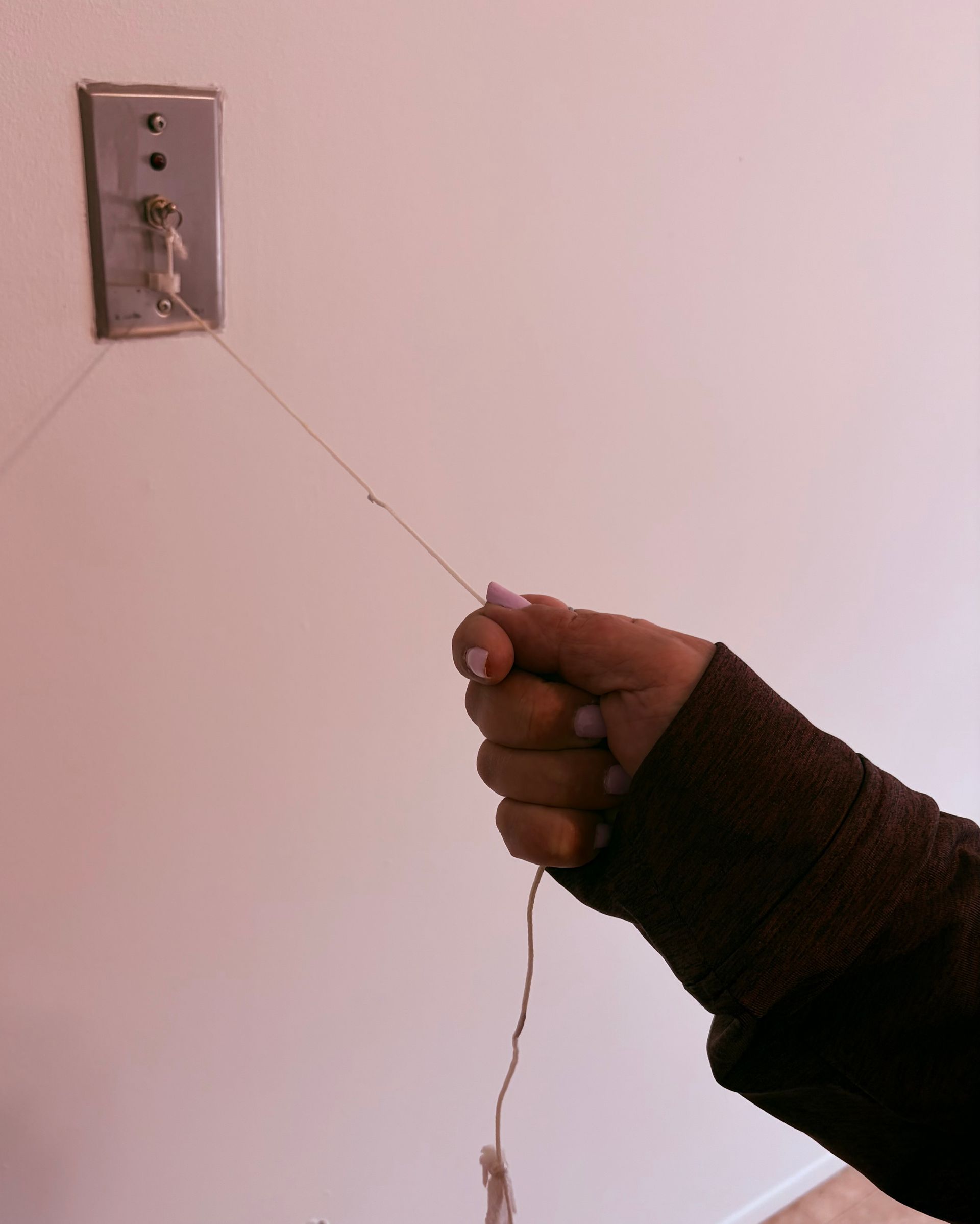A person’s hand pulls a thin string attached to a light-colored wall-mounted switch plate.