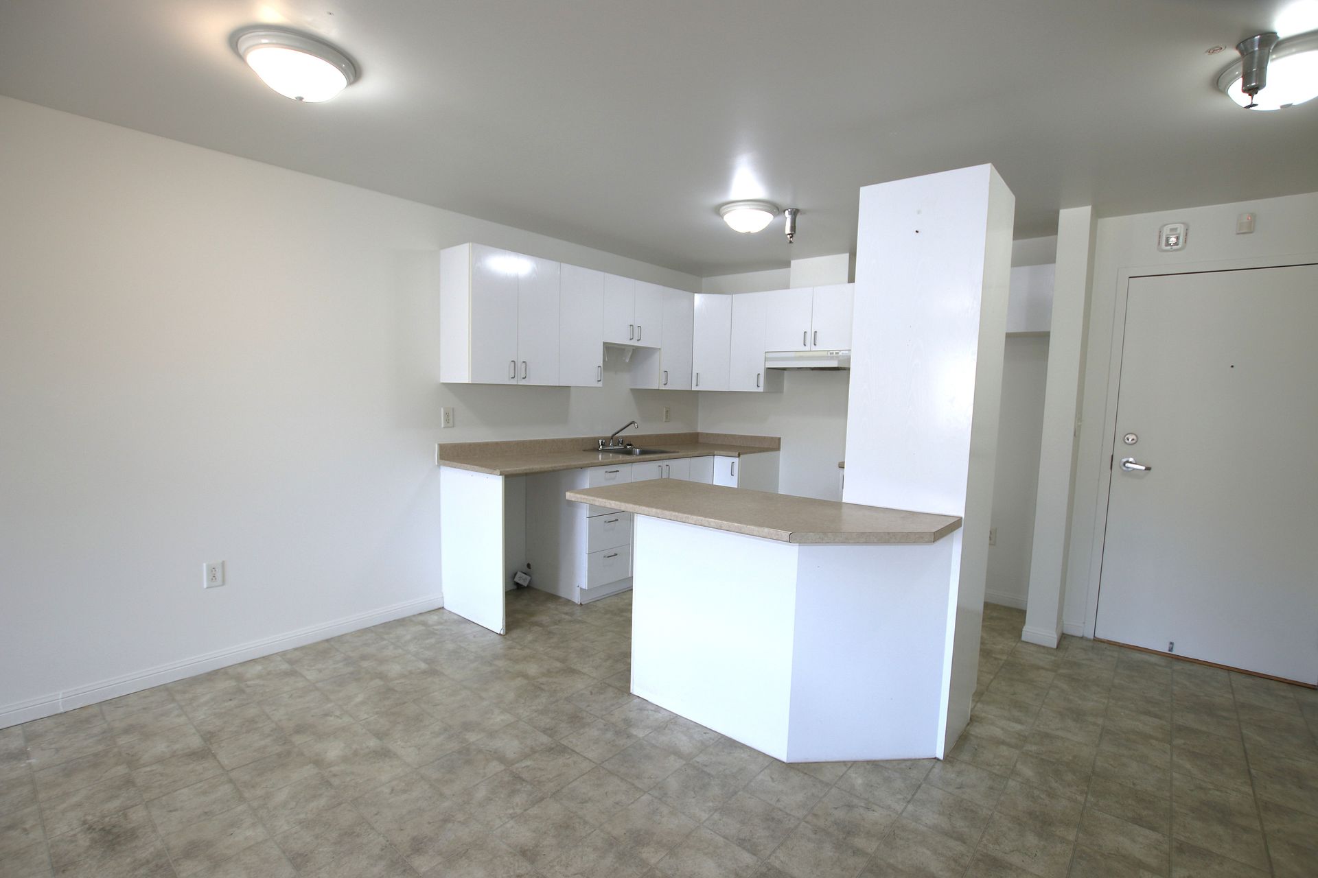 A bright kitchen with white cabinets, light-colored countertops, a breakfast bar, and tile flooring.