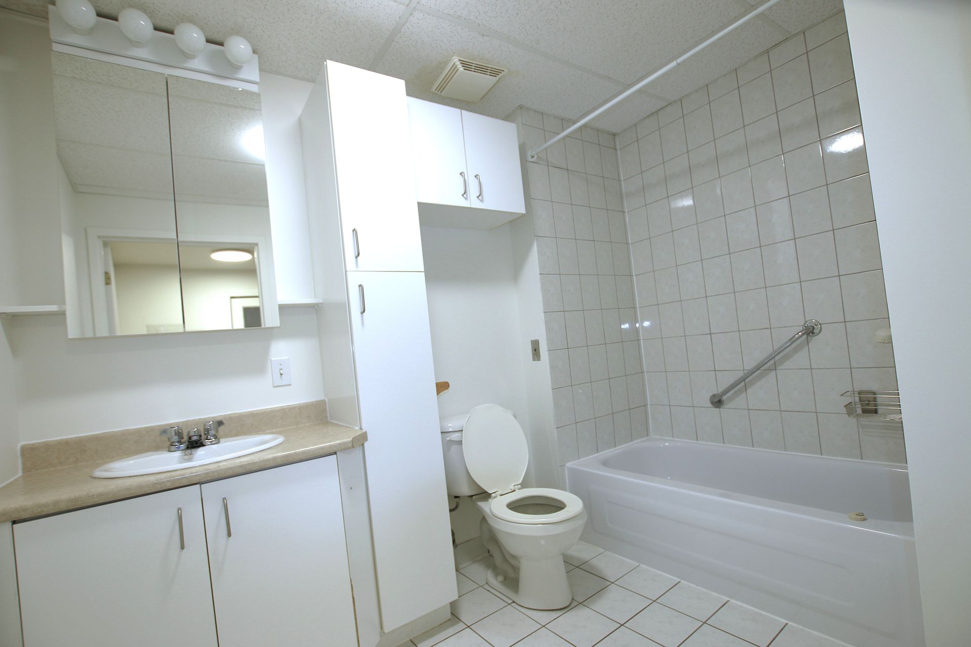 A white bathroom featuring a vanity with a sink, a toilet, and a bathtub with a tiled surround and a grab bar.