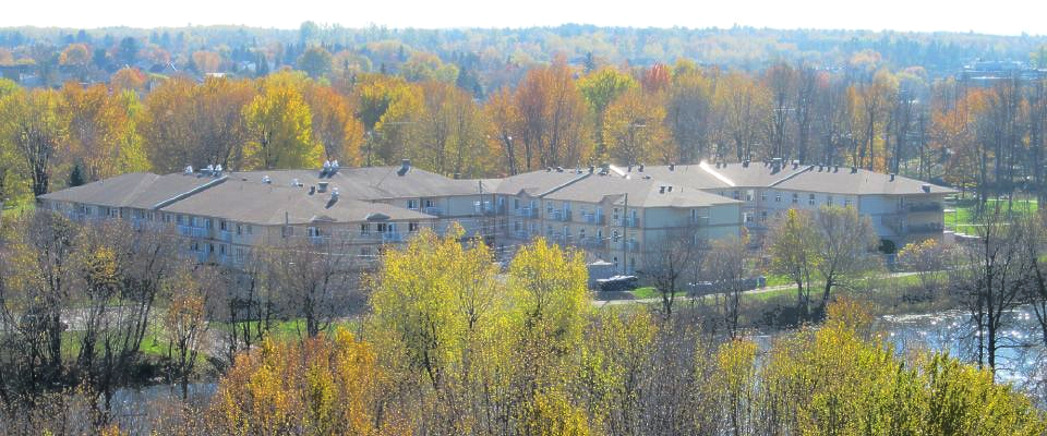 An aerial view of a multi-story apartment complex surrounded by lush trees with autumn-colored fall foliage.