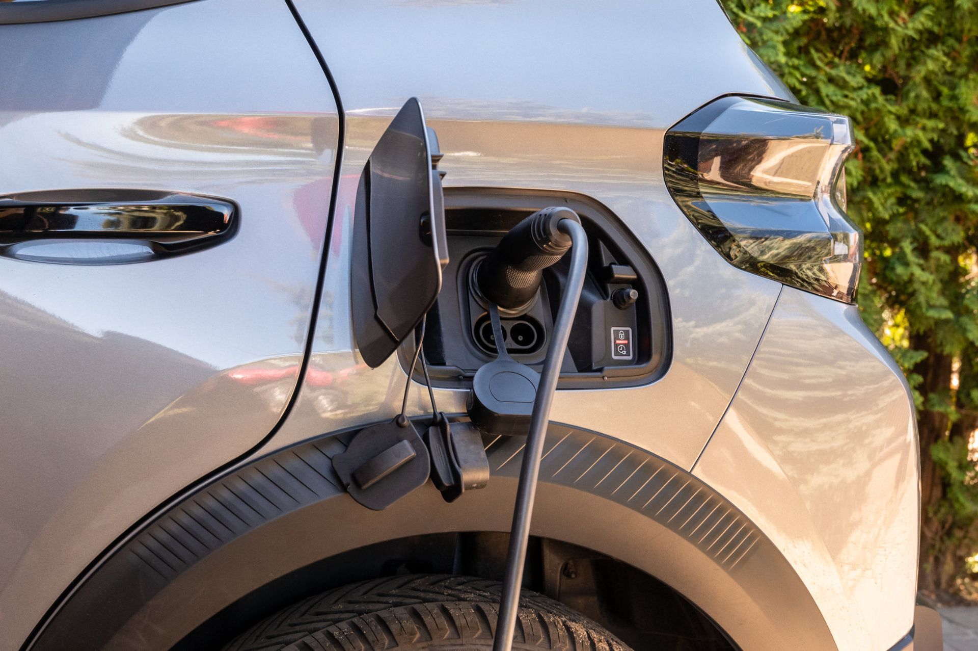 Electric car charging at a curb, with the charging port open on a silver vehicle.