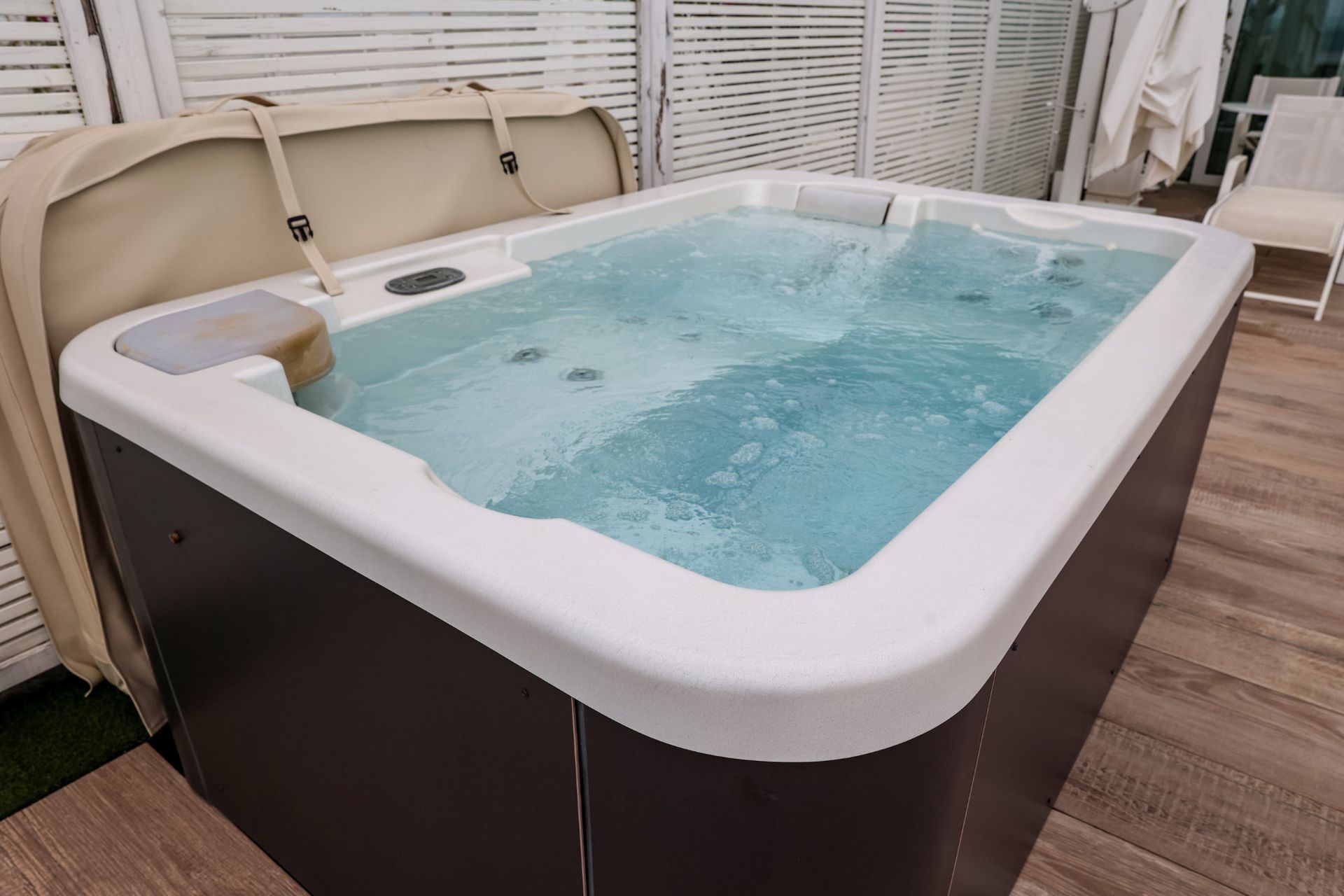 Inflatable hot tub filled with water on a wooden deck, with the cover partly open