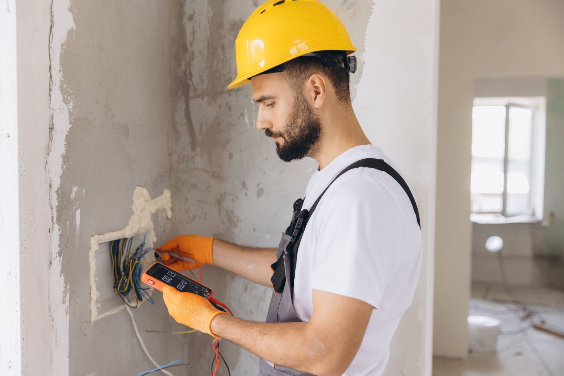 Electrician in yellow hard hat wiring a wall outlet in a renovated room