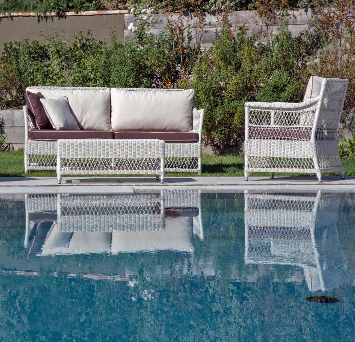Mobili da esterno in vimini bianco disposti vicino alla piscina; cuscini beige e dettagli marroni.