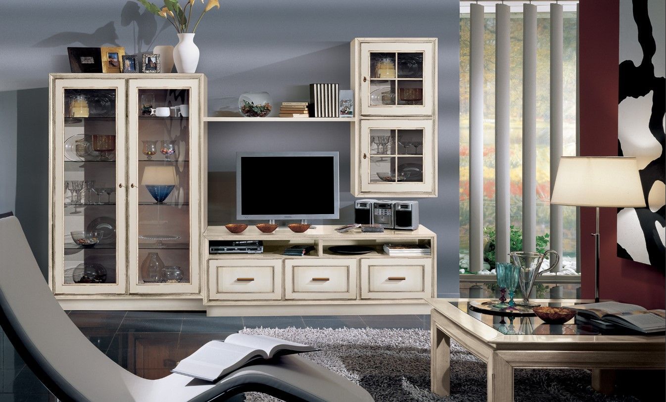 Soggiorno con mobile TV in legno color crema, TV e vetrine. In primo piano, poltrona e tavolino.