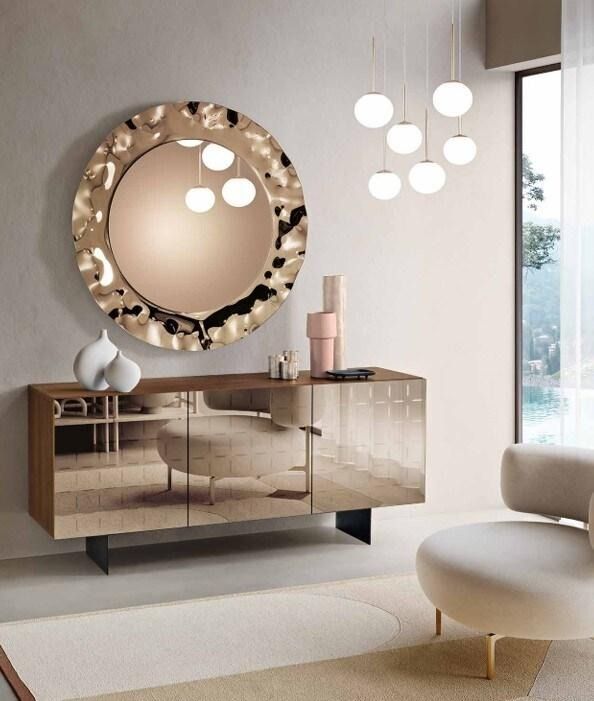 Credenza con specchio e lampada. Uno specchio rotondo e strutturato è appeso sopra una credenza a specchio.