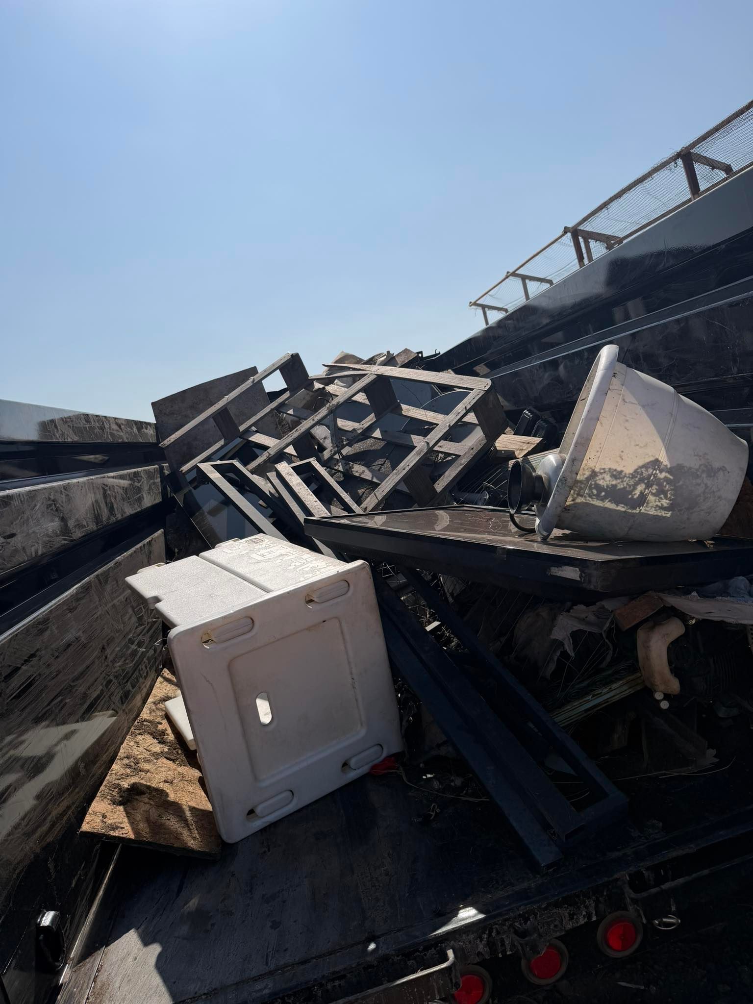 Collapsed metal debris on a flatbed truck under a clear blue sky, with a white utility box in the foreground.