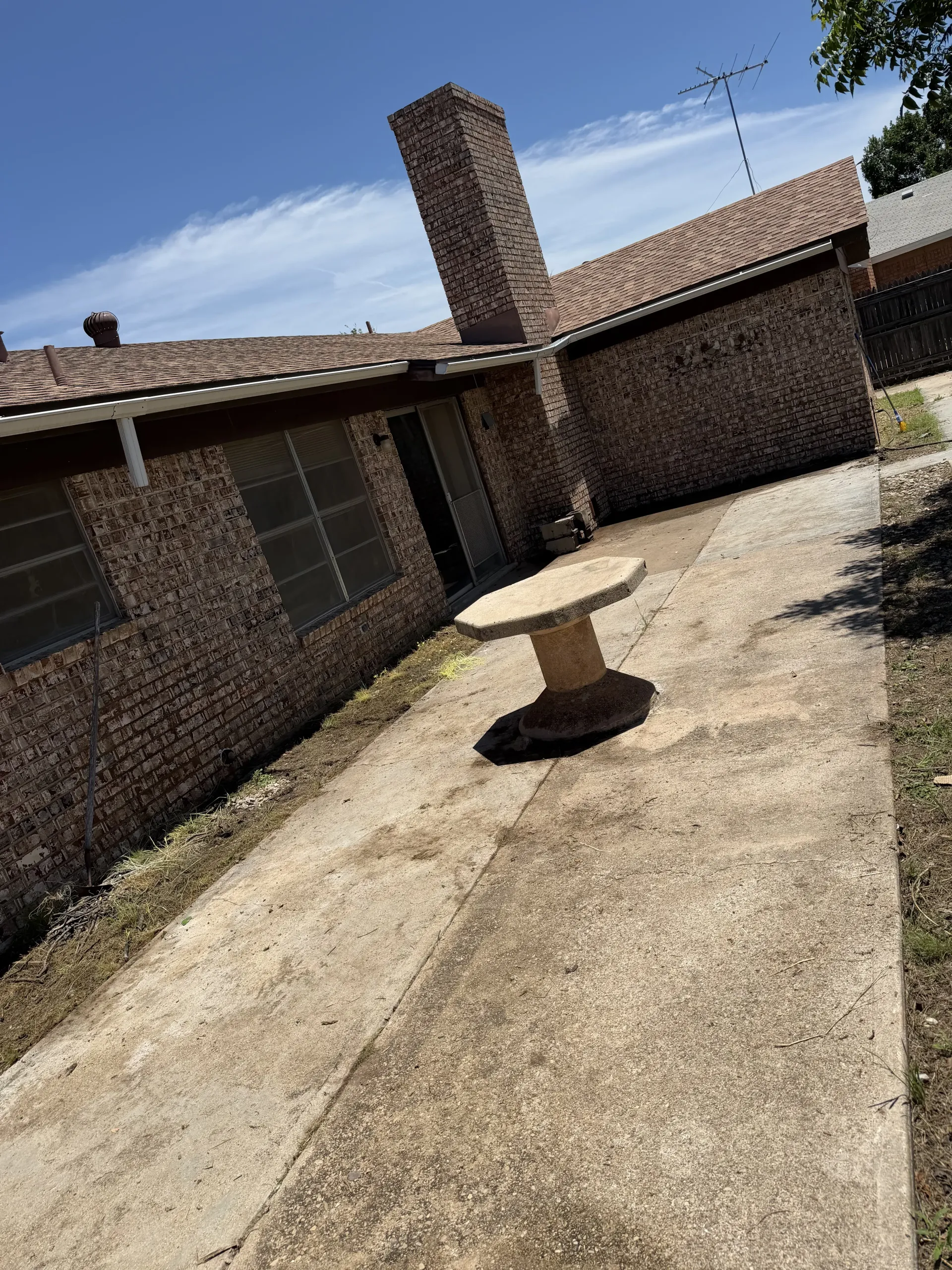 Sunlit brick patio with a small round table and a chimney beside a house