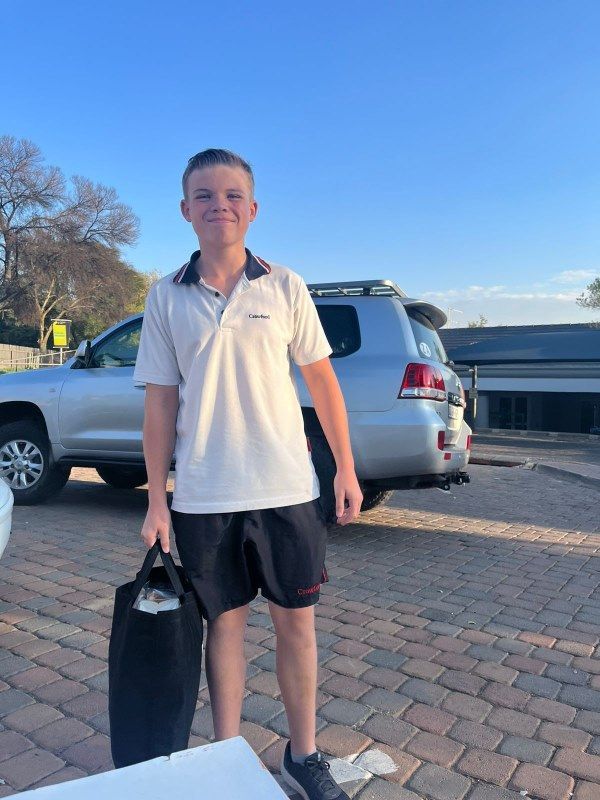 A young boy is standing in front of a silver suv holding a black bag.
