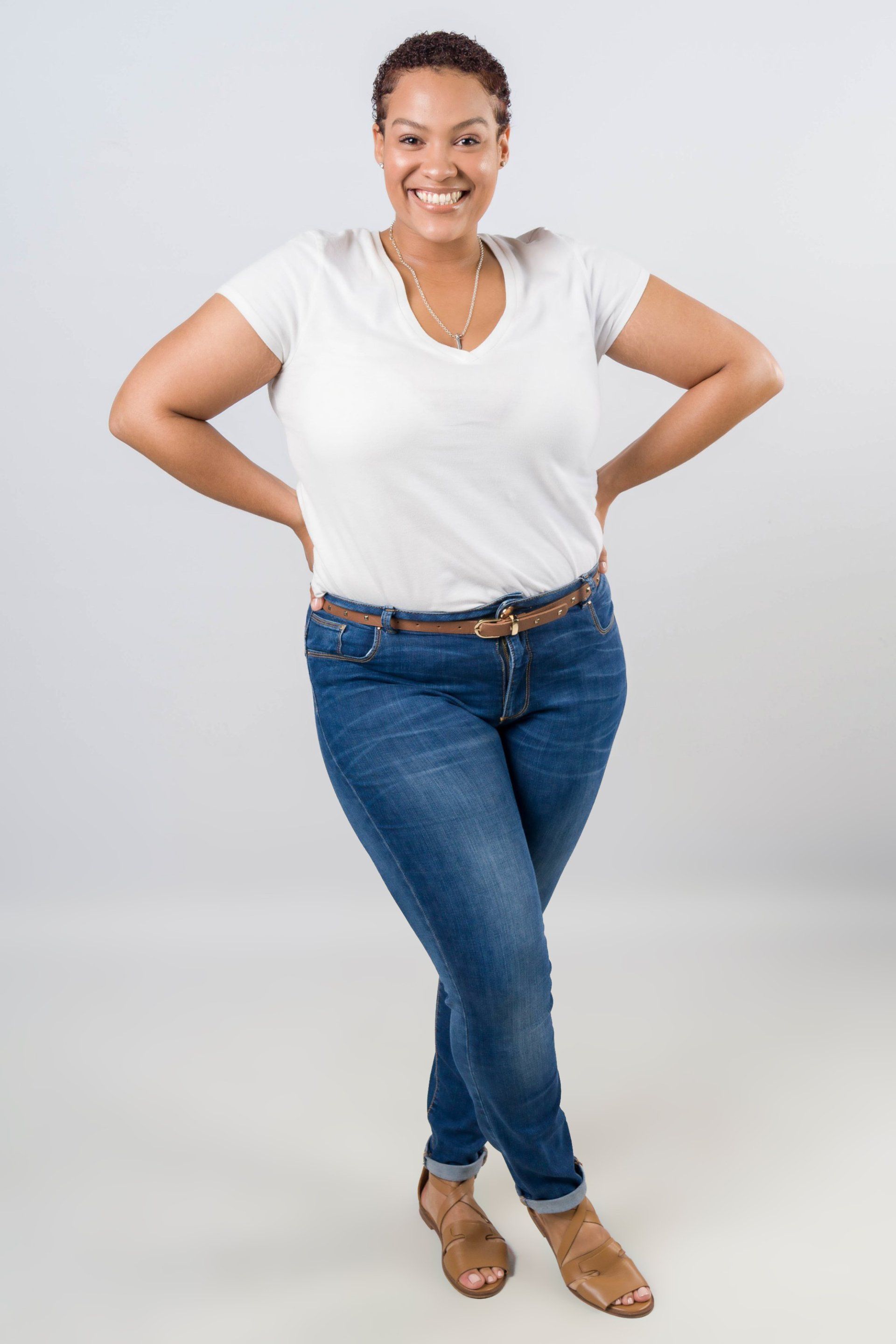 A woman in a white shirt and blue jeans is standing with her hands on her hips.