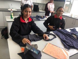 Two girls are sitting at a table in a kitchen cutting clothes.