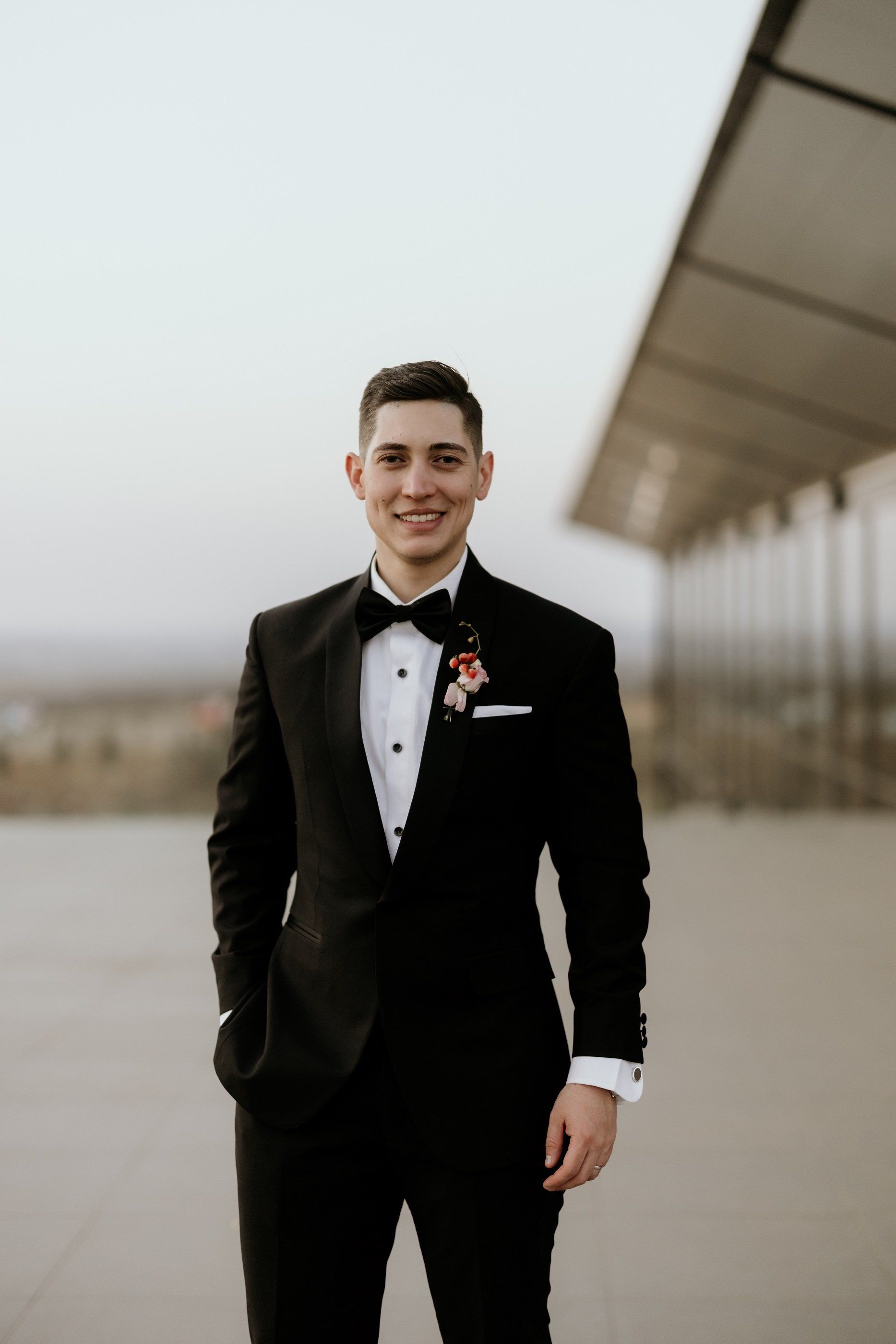 A man in a tuxedo and bow tie is standing in front of a building.