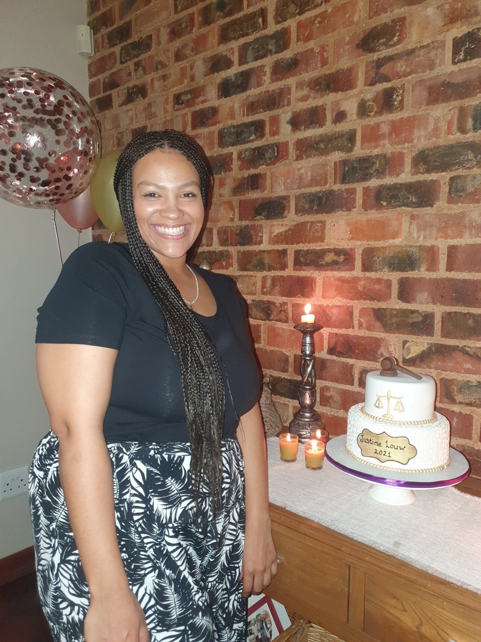 A woman is standing in front of a cake and balloons.
