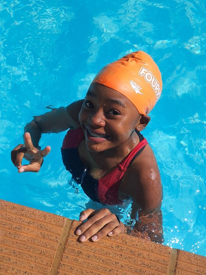 A young girl wearing an orange swim cap is swimming in a pool.