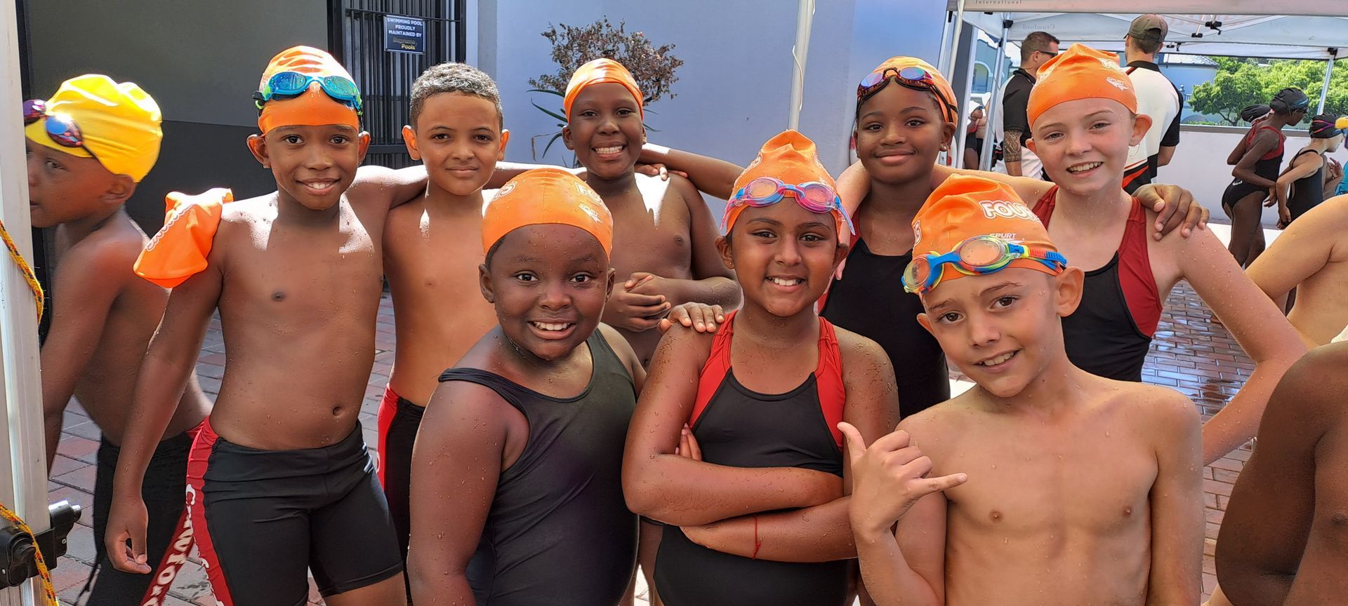 A group of young children wearing orange swim caps and goggles are posing for a picture.