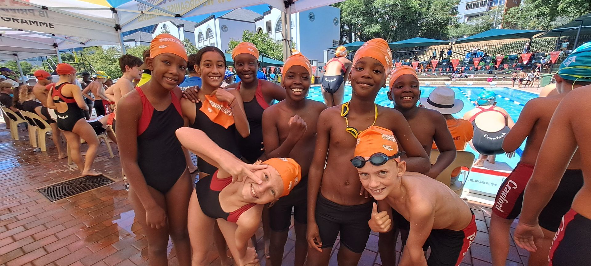 A group of young swimmers are posing for a picture in front of a swimming pool.