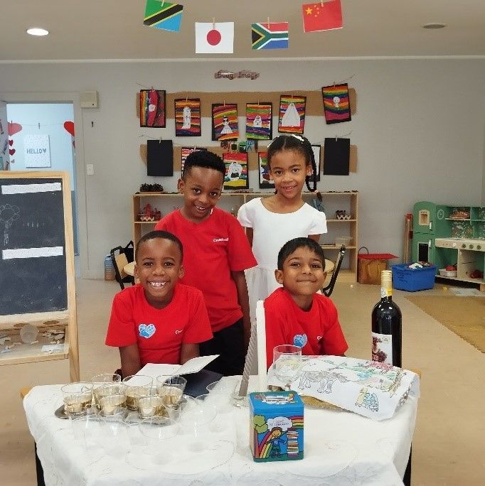 A group of children standing around a table with a bottle of wine