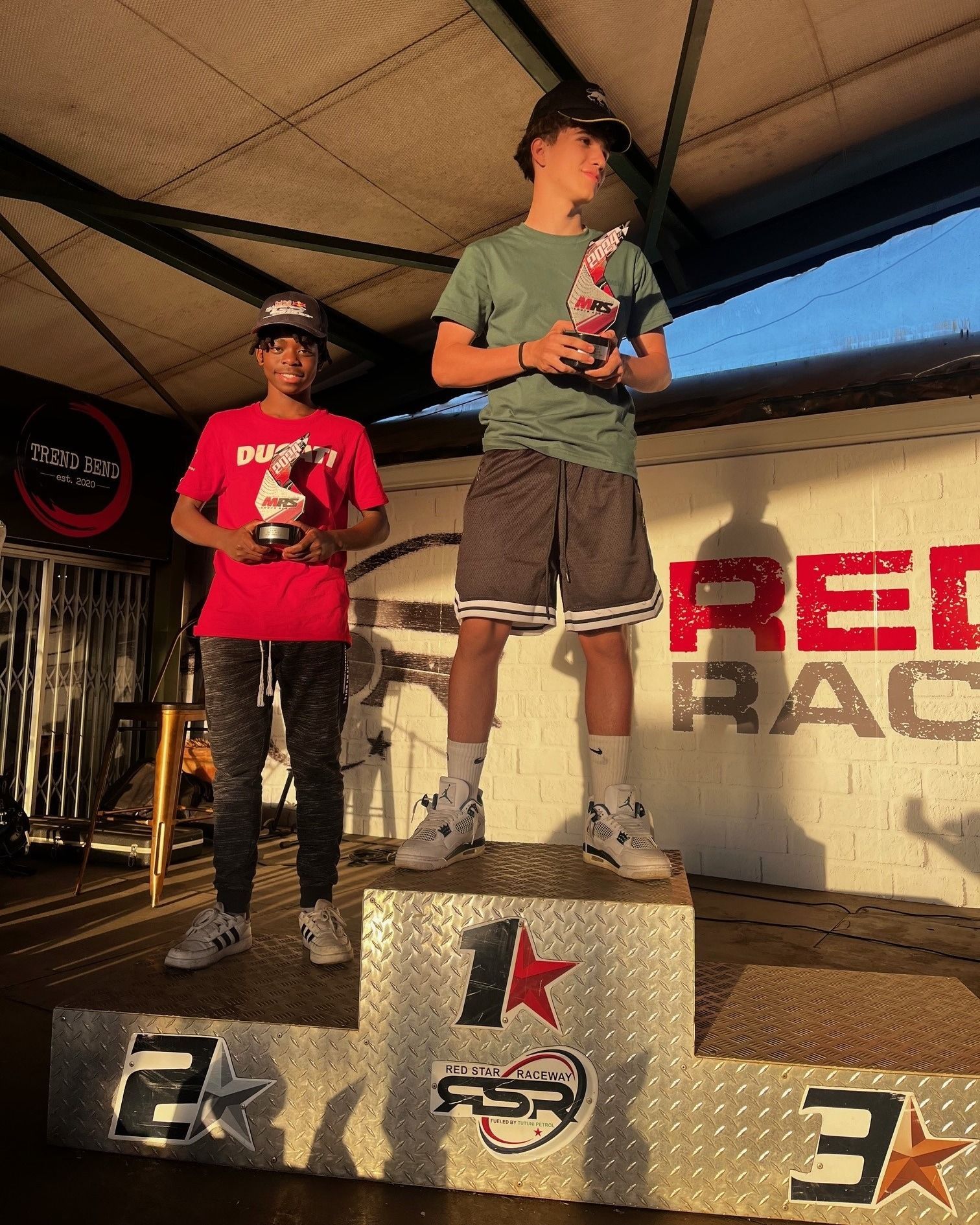Two young men are standing on a podium holding trophies.