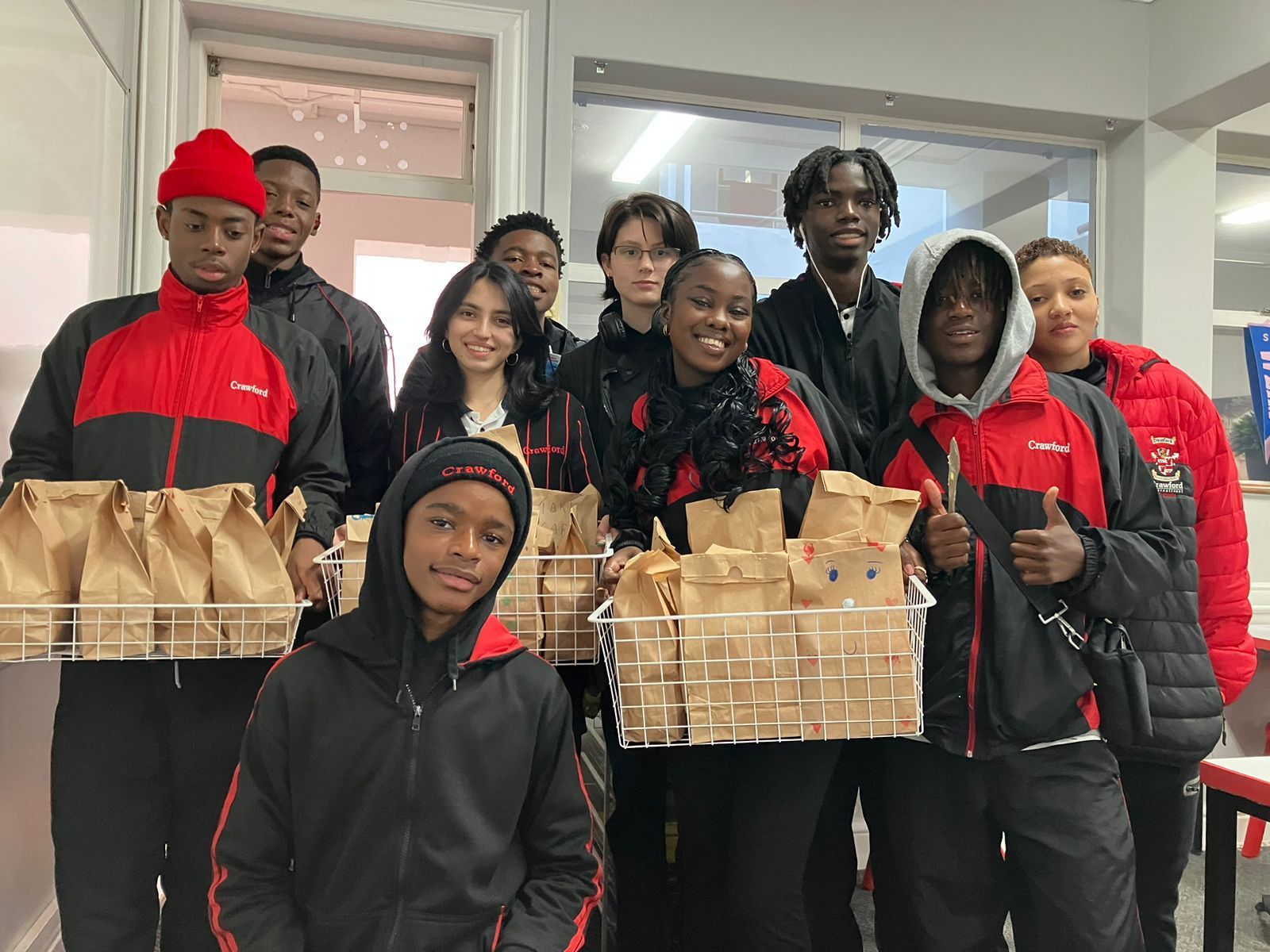 A group of young people are standing next to each other holding bags of food.