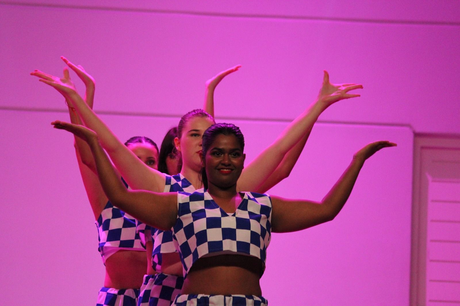 A group of women are dancing on a stage with their arms outstretched.