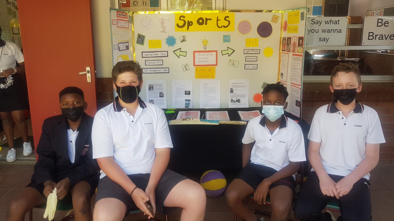 A group of children wearing face masks are sitting in front of a board that says sports