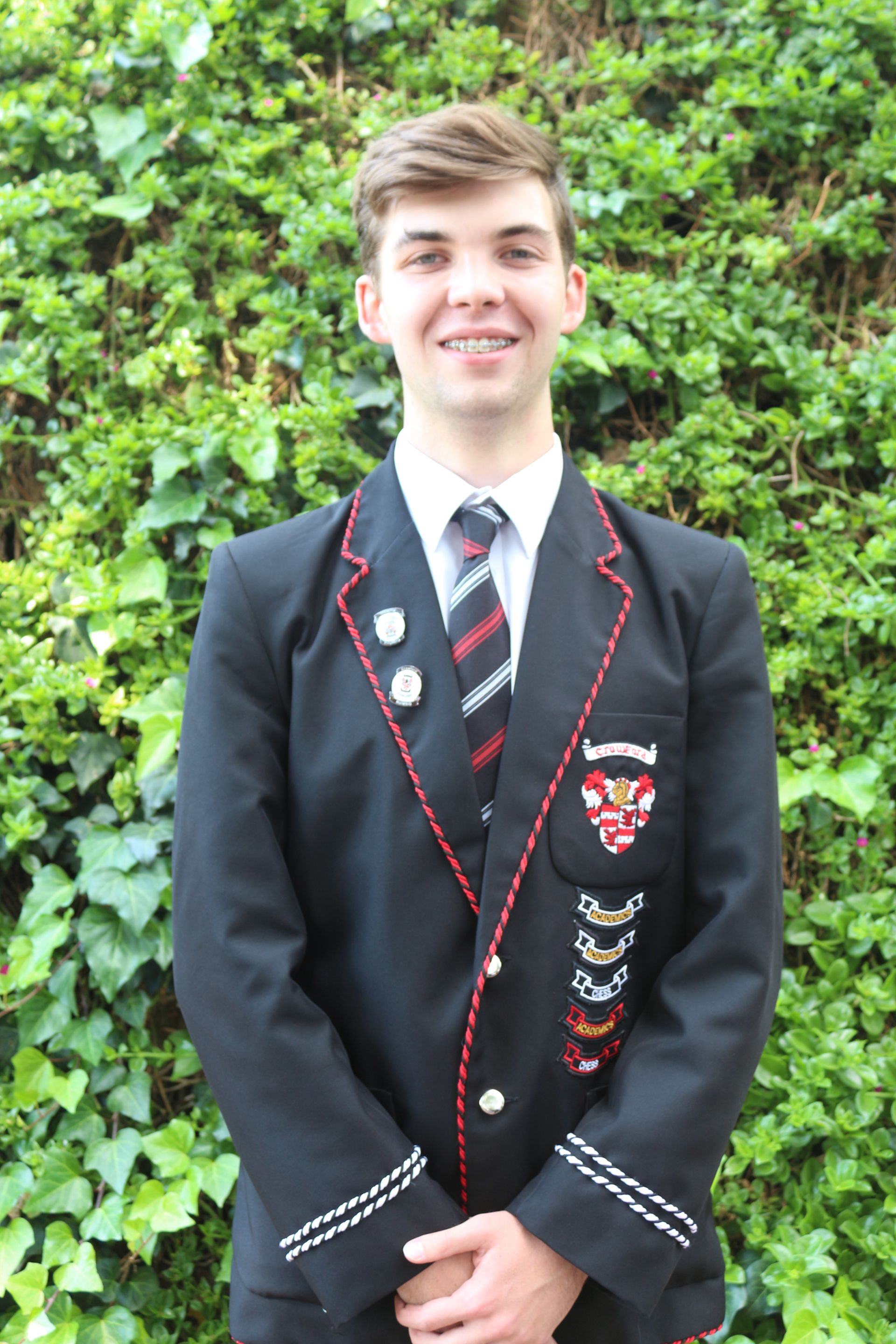 A young man in a suit and tie is standing in front of a bush.