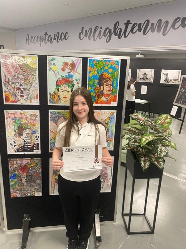 A young girl is standing in front of a wall of paintings holding a certificate.