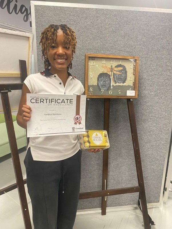 A woman is holding a certificate in front of a painting on an easel.