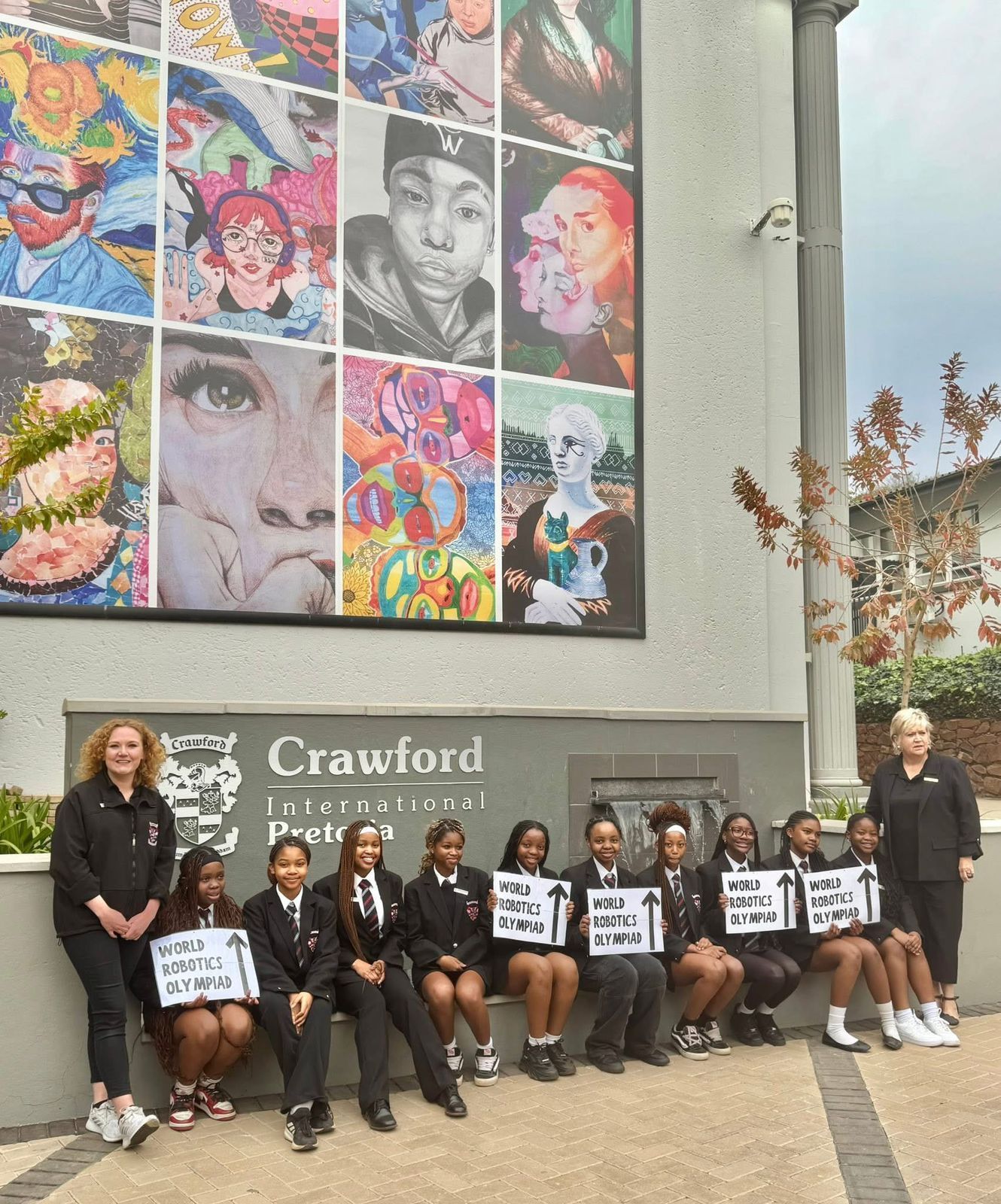 Group of students with signs in front of a mural and building. Crawford International.