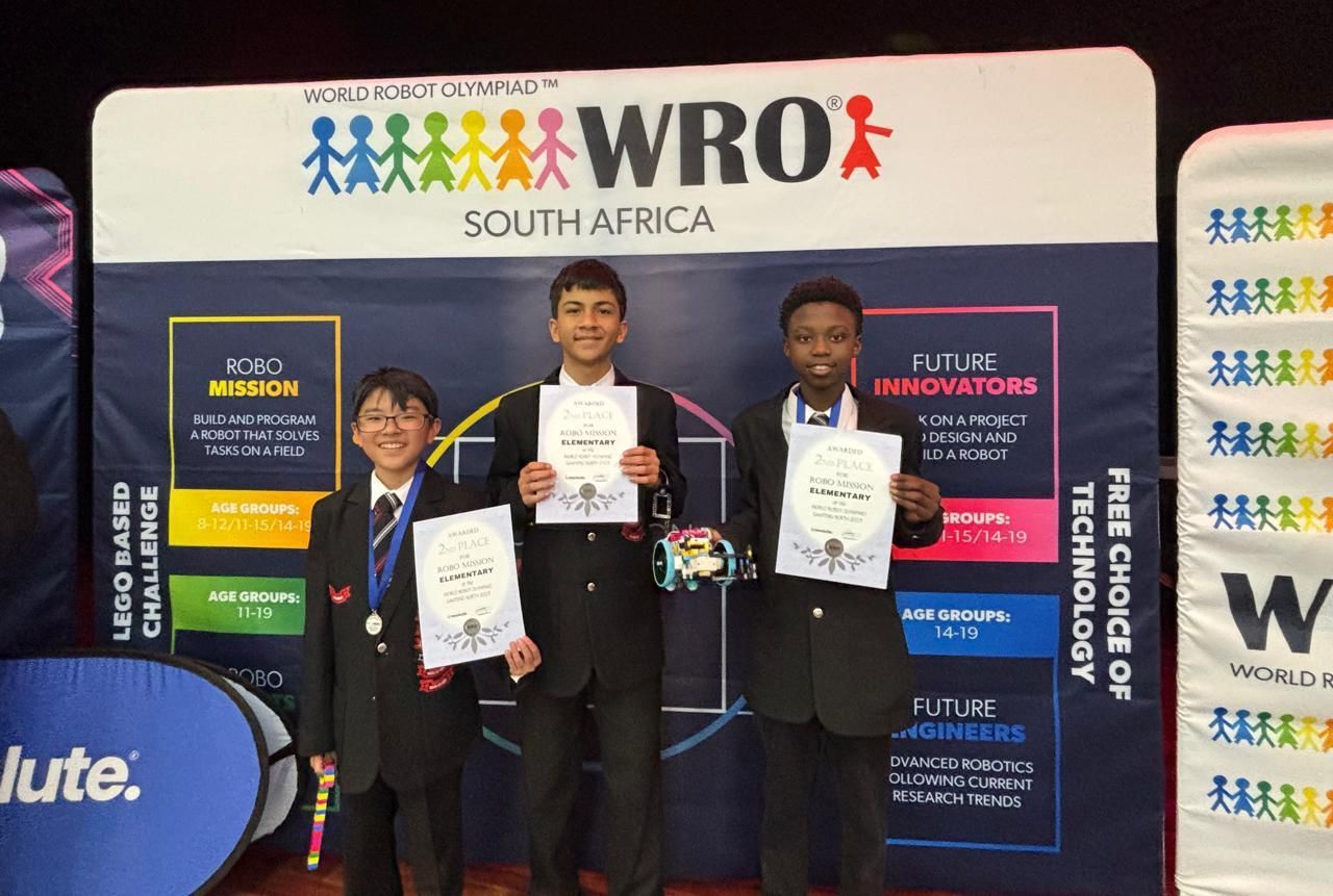 Three students in formal attire hold certificates in front of a WRO South Africa banner.