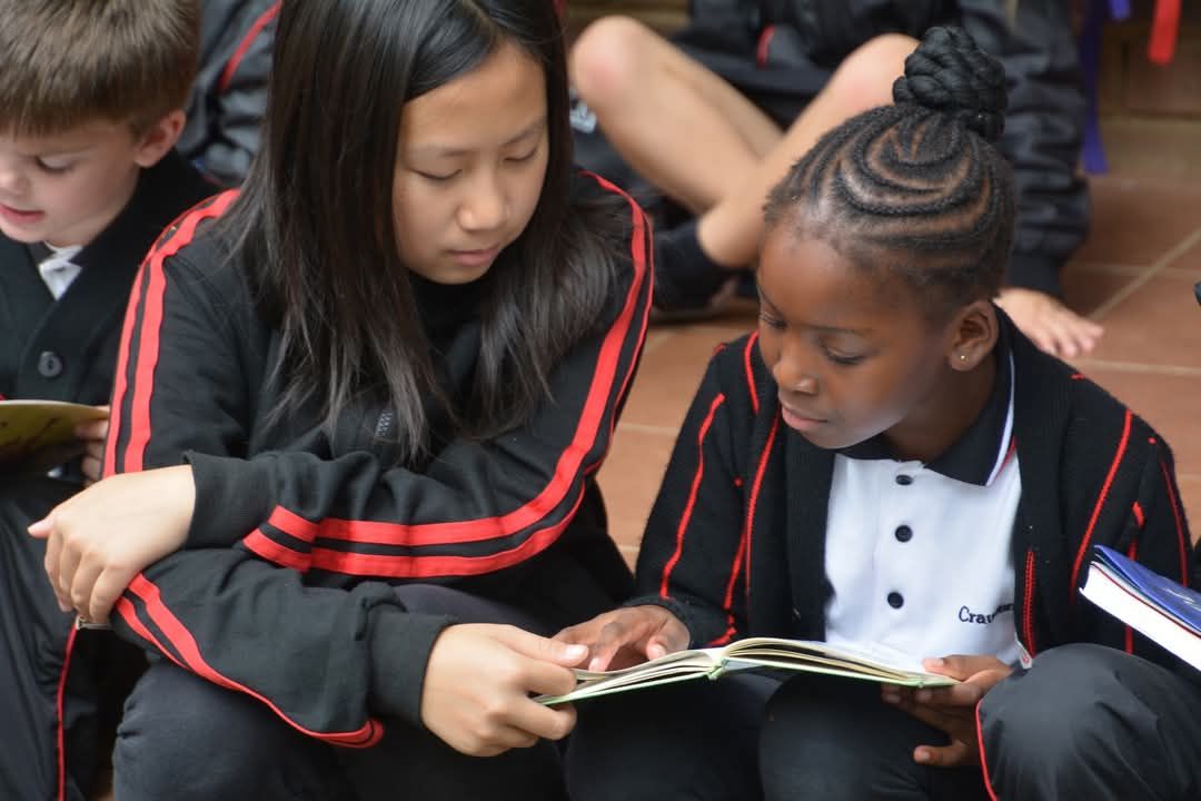 Two students in school uniforms reading a book together, outside.