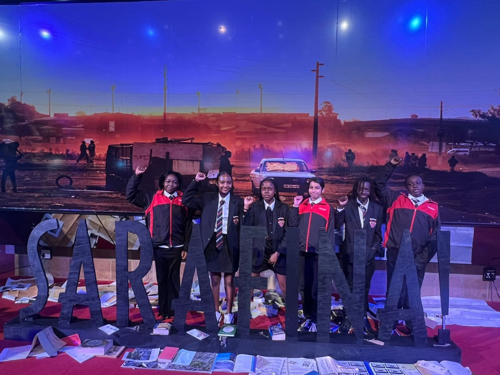 Group of people in jackets pose in front of a stage backdrop of an urban landscape and large lettered word