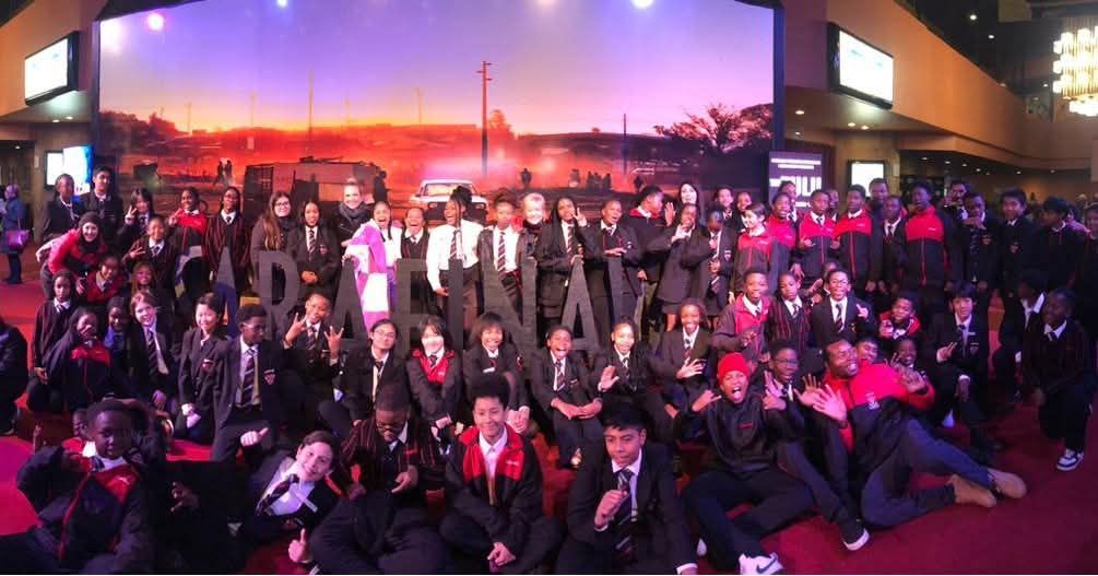 Large group of people in formal attire, posing in front of a stage with a sunset backdrop.