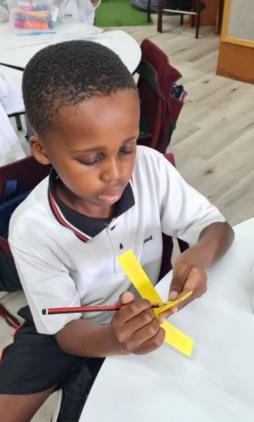 A young boy is sitting at a table with a pencil and a yellow piece of paper