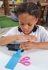 A young girl is sitting at a table cutting a piece of blue paper with scissors.